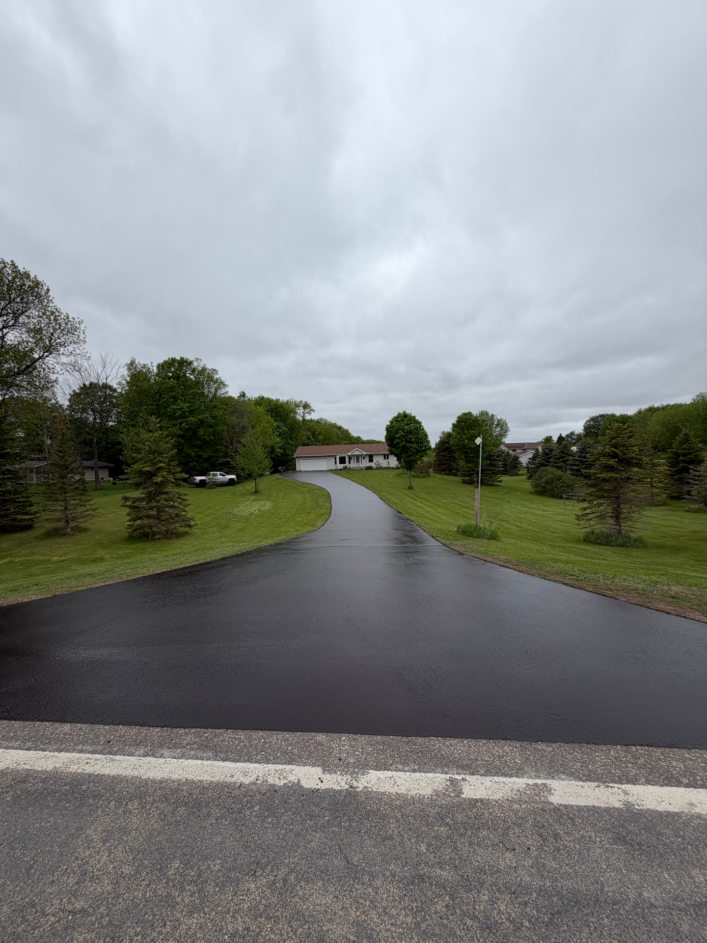 Same long curved residential driveway after seal coating with a deep black finish