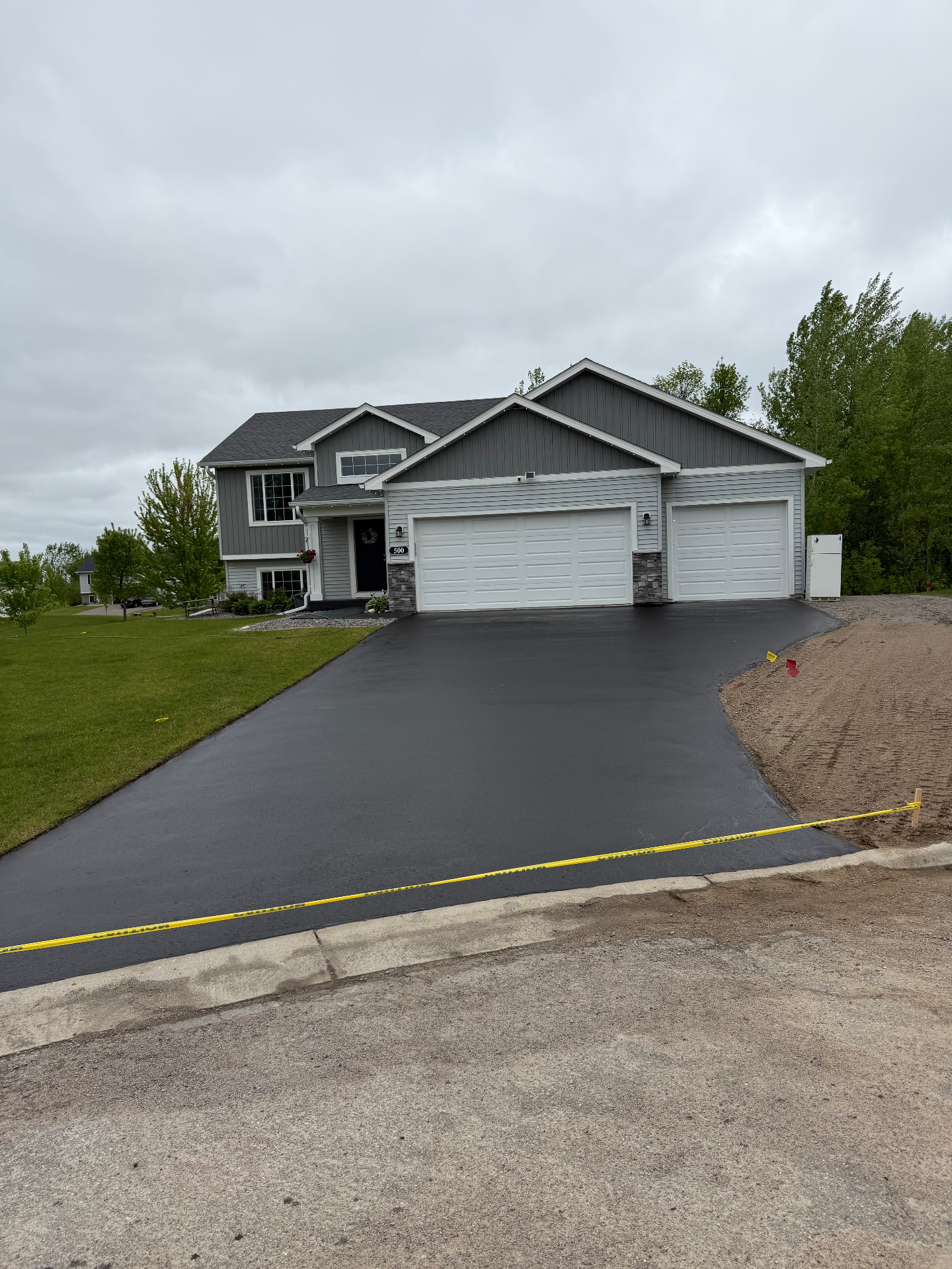 Freshly paved wide residential driveway in front of a gray split-level home