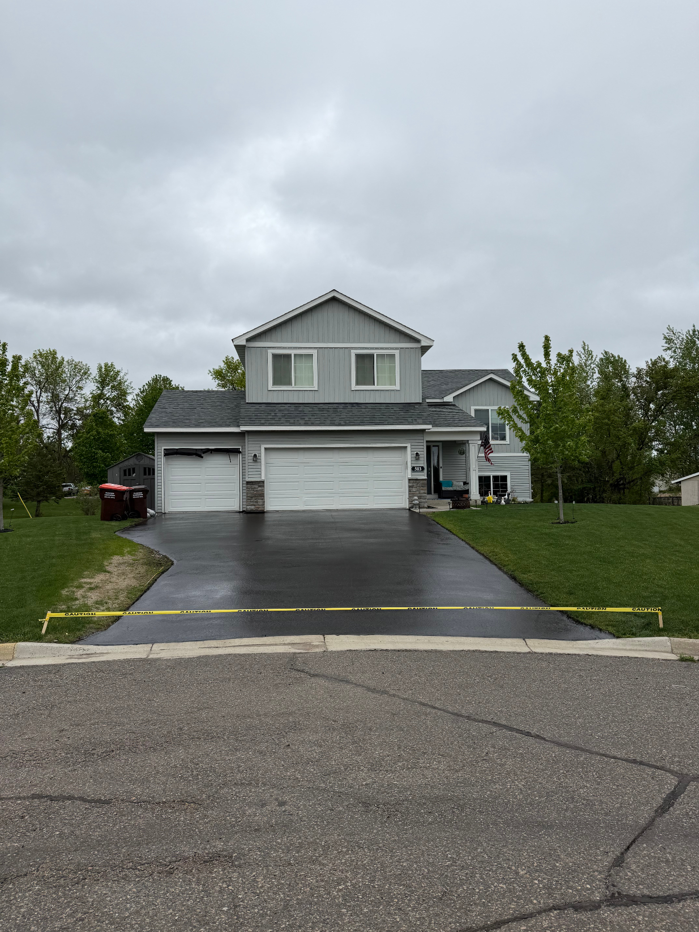Freshly sealed driveway in front of a gray two-story home on an overcast day