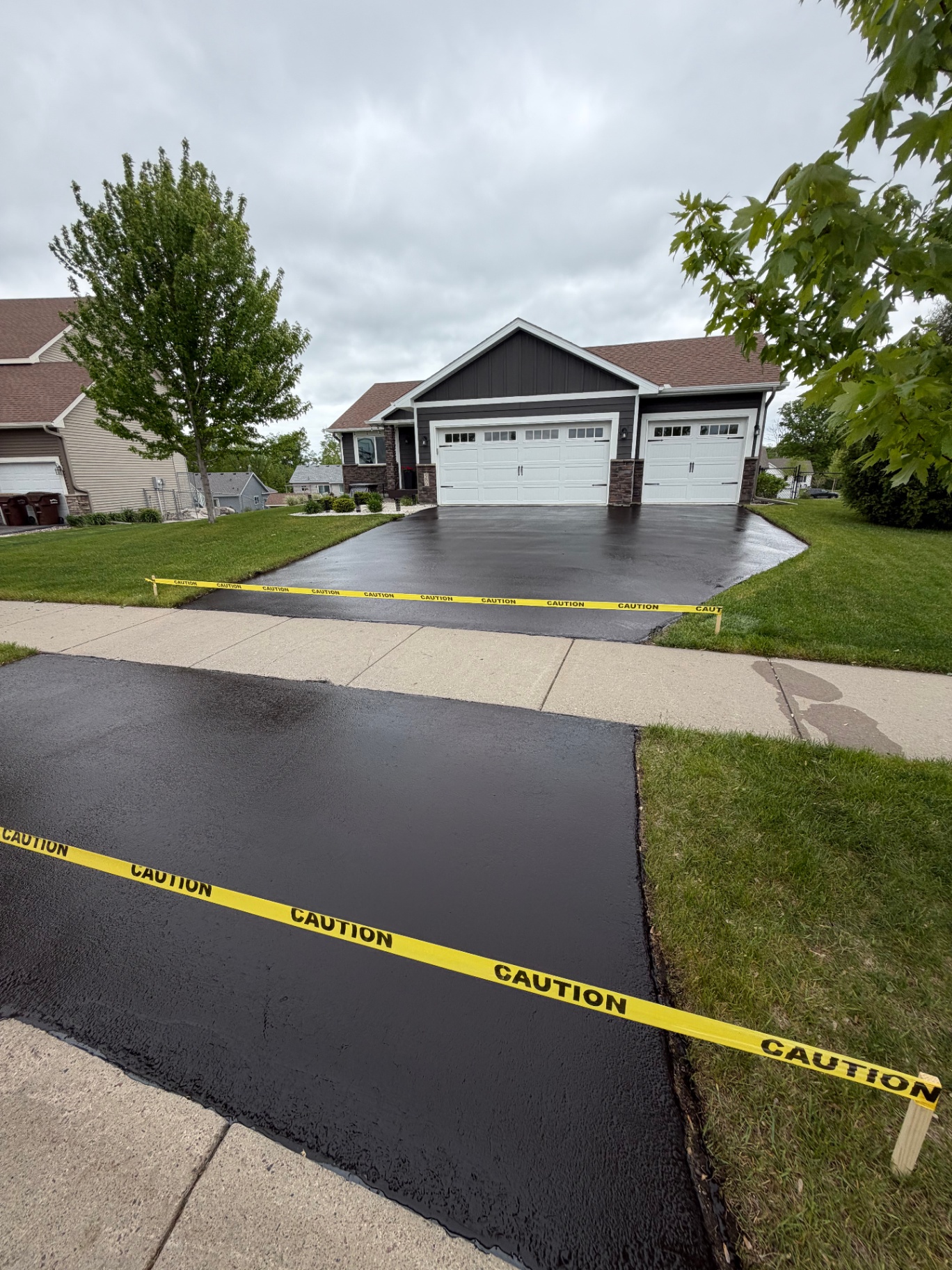 Freshly sealed driveway leading to a dark-sided home with bright white garage doors